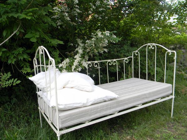 Un lit en fer blanc placé sous les arbres
